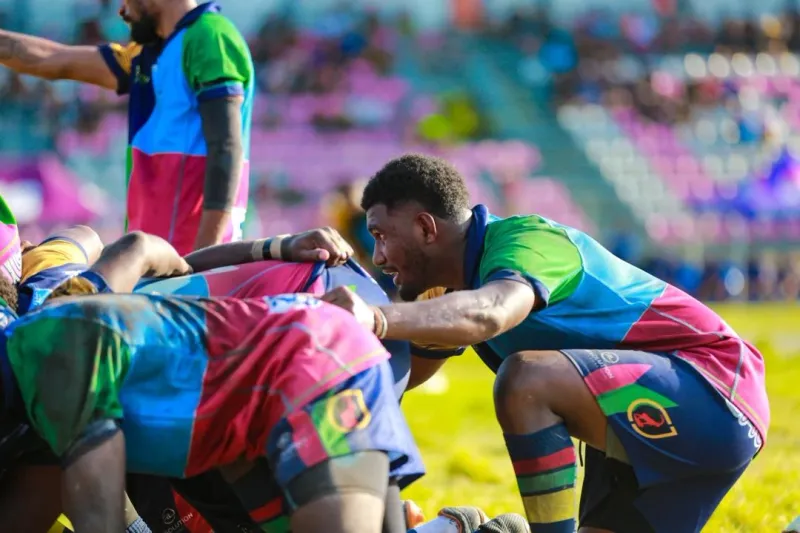 A rugby player crouching beside his teammates' scrum during a match