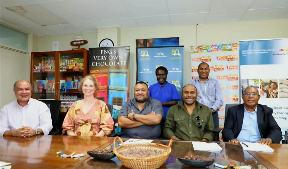 A group seated around a meeting table with bowls of cocoa beans, in front of Paradise Foods banners
